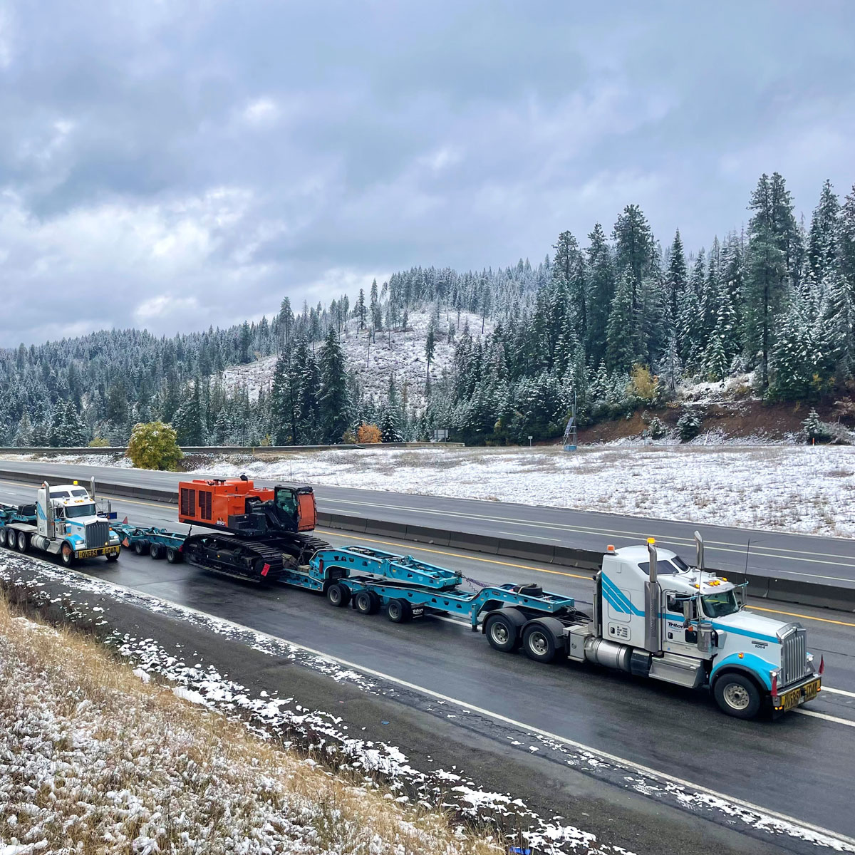 Heavy haul truck transporting equipment through a snowy mountain highway.