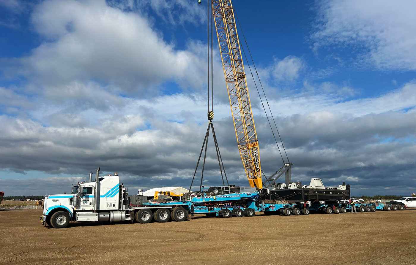 Triton Transport specialized trailer and crane loading operation at an industrial site.
